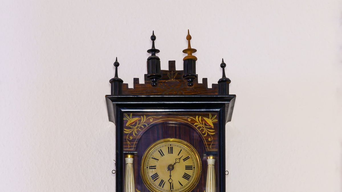 Ornate wooden wall clock with Roman numeral dial showing the time